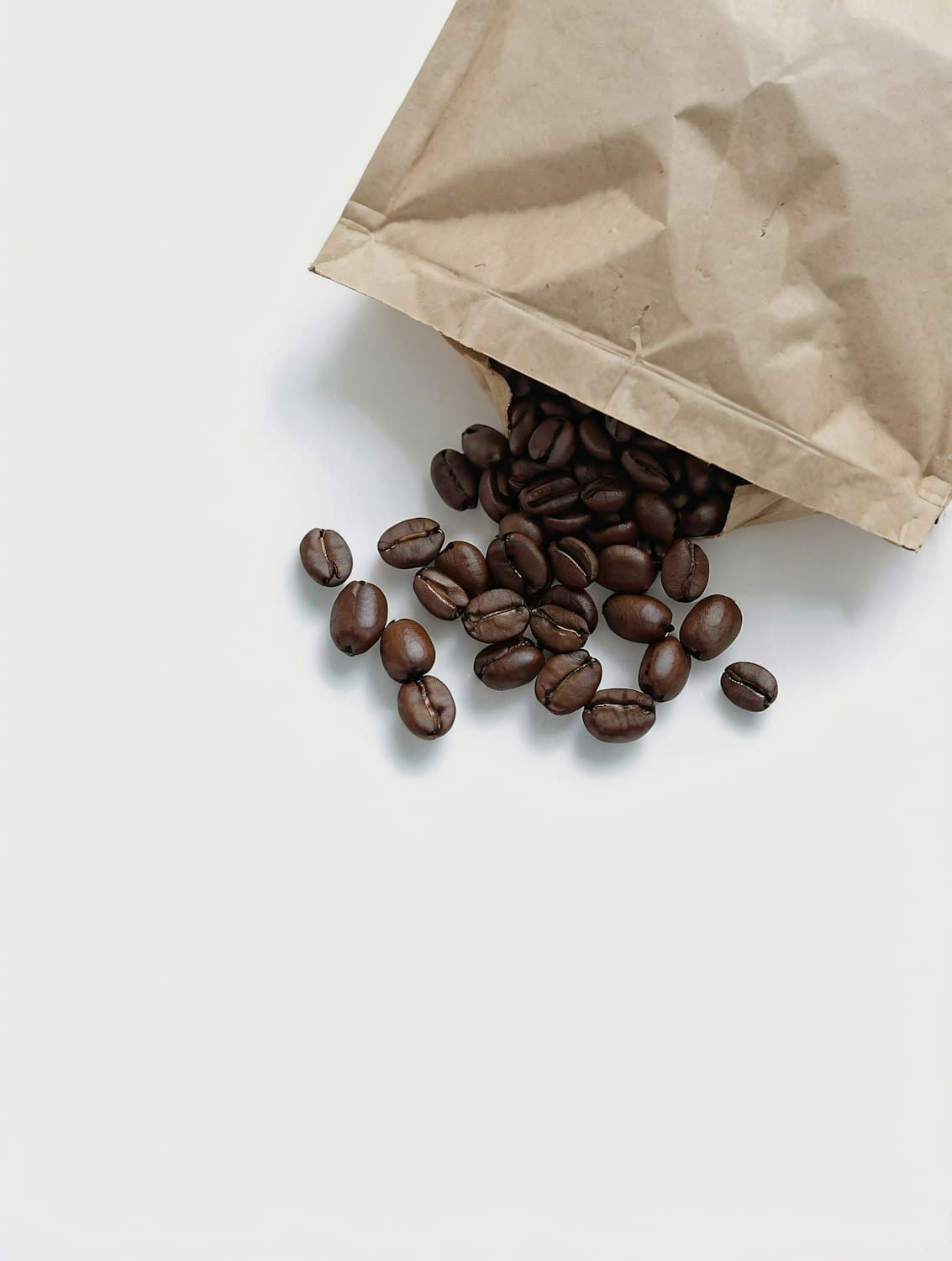Paper bag of Kin coffee spilling dark roasted beans onto a white table